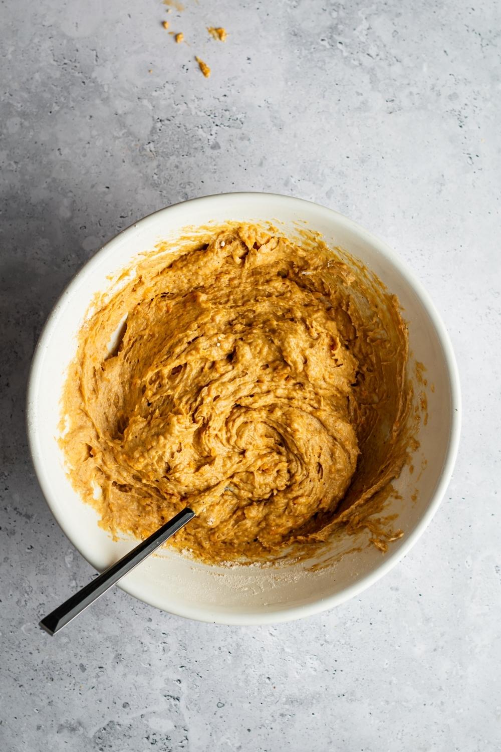 Sweet potato pound cake batter with a spoon in it in a white bowl.