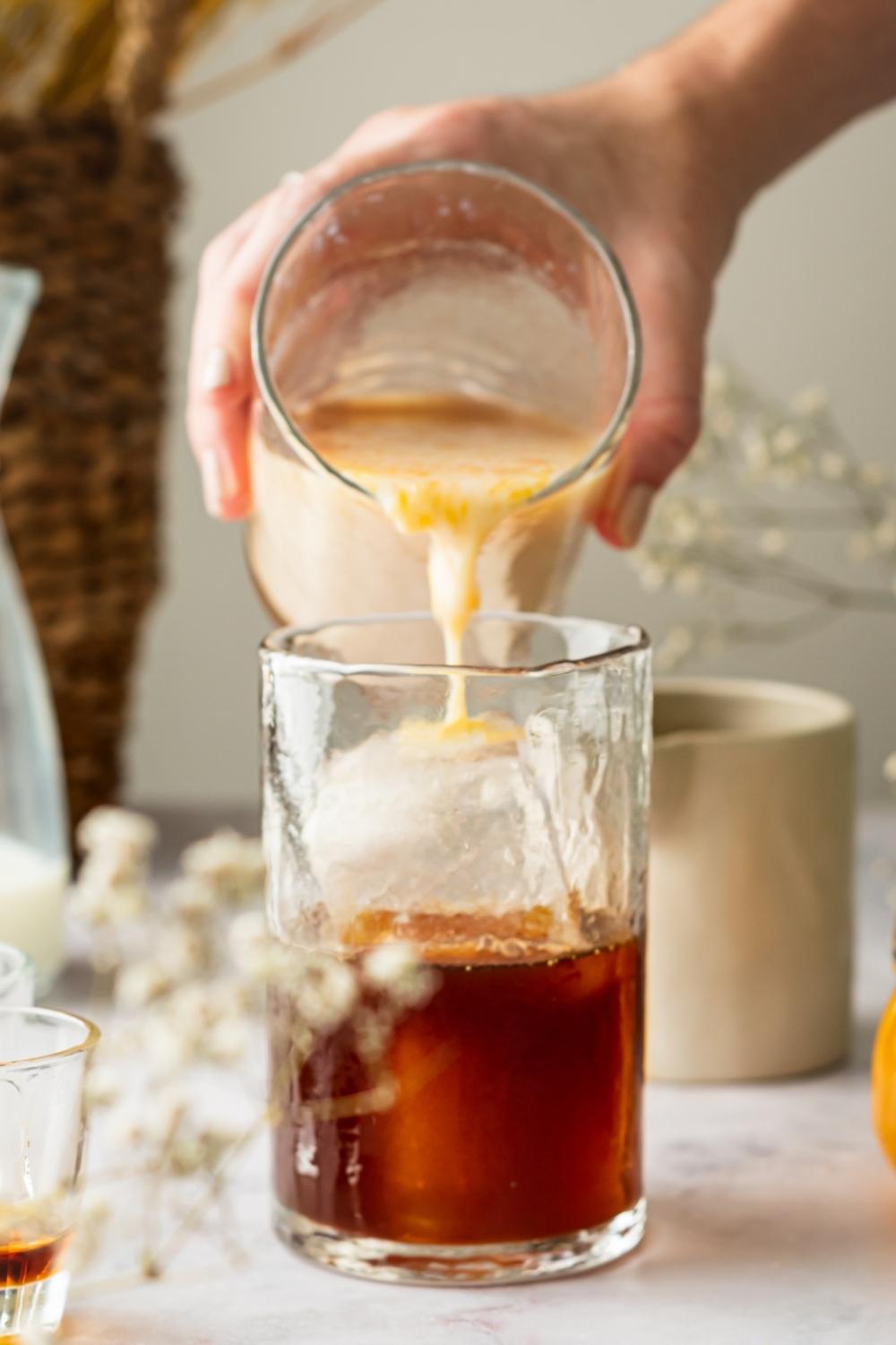 A hand pouring pumpkin cold foam into a glass of ice and cold brew coffee.