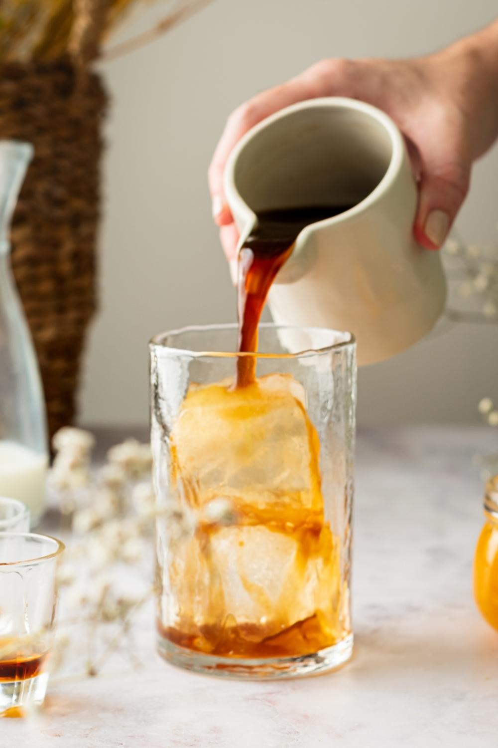 A hand pouring cold brew coffee into a glass of ice.