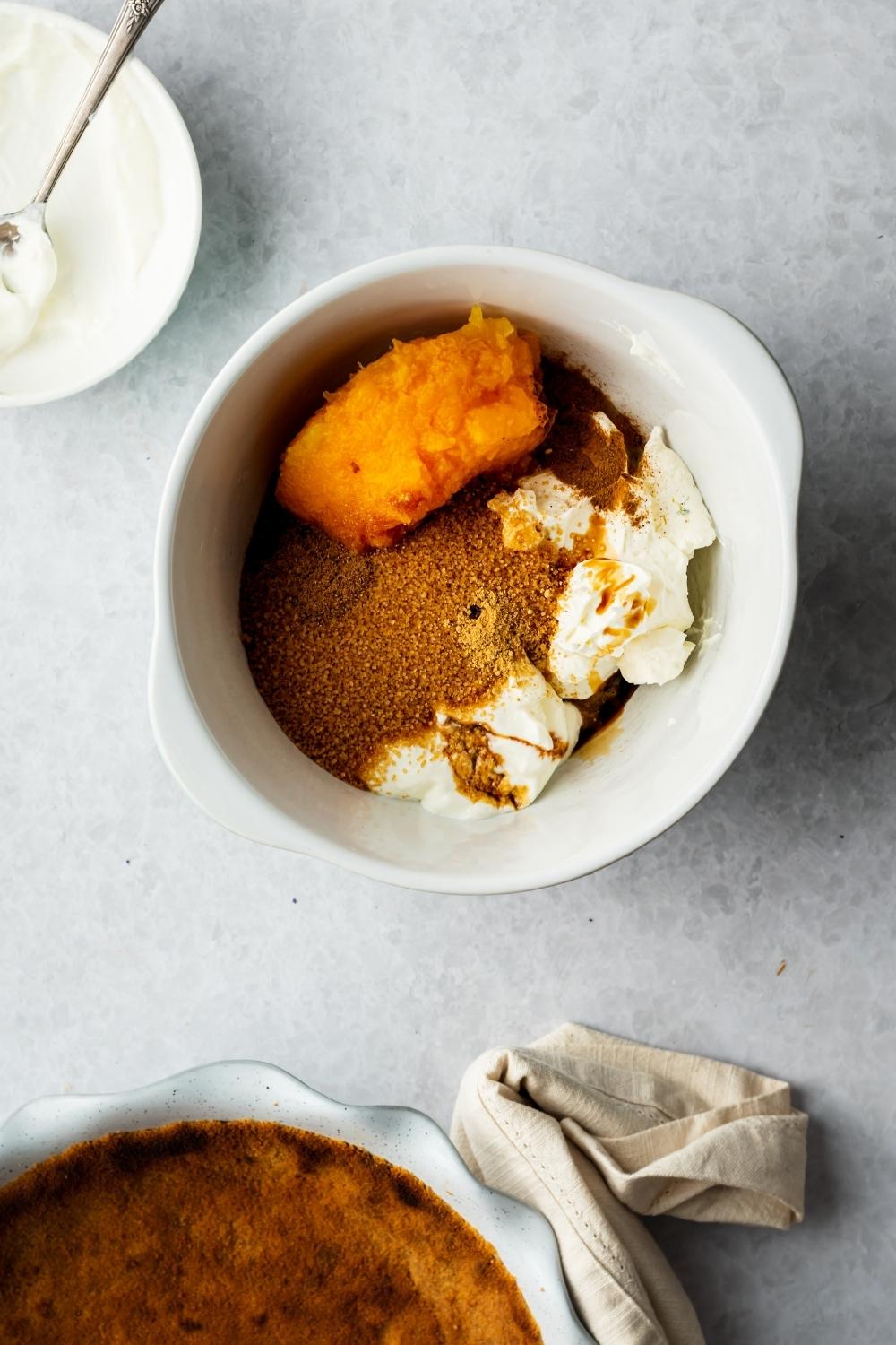 Pumpkin puree, brown sugar, cream cheese, and other ingredients in a white bowl.