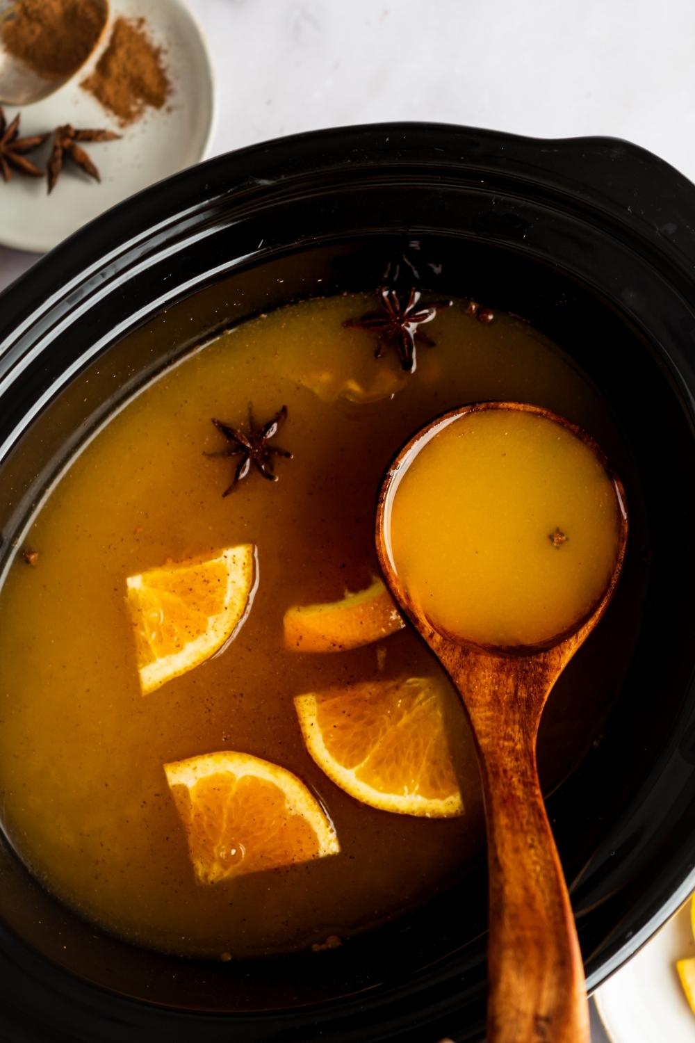 A ladle scooping russian tea out of a crock pot filled with the russian tea.