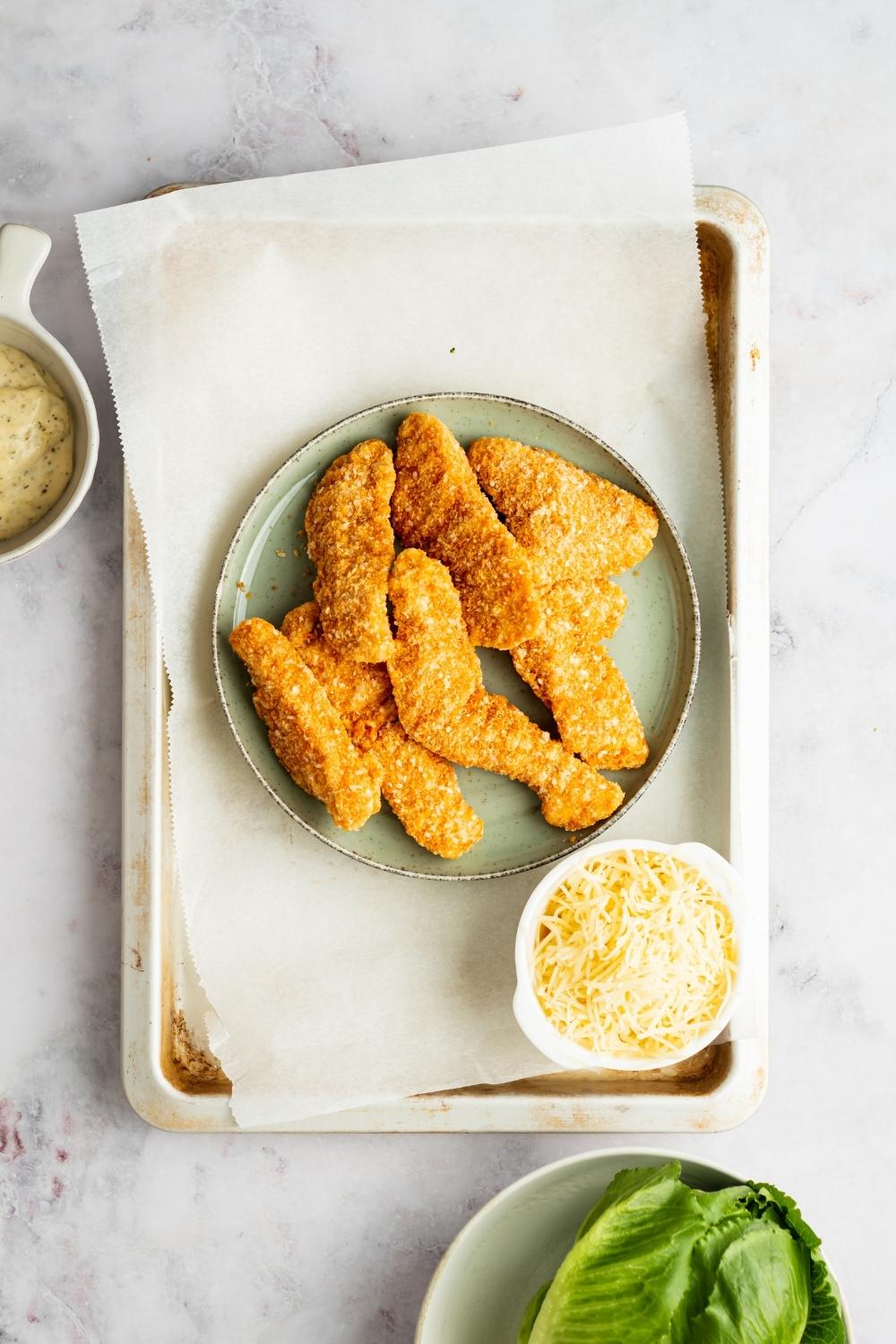 baked chicken tenders on a plate next to a small bowl of shredded cheese