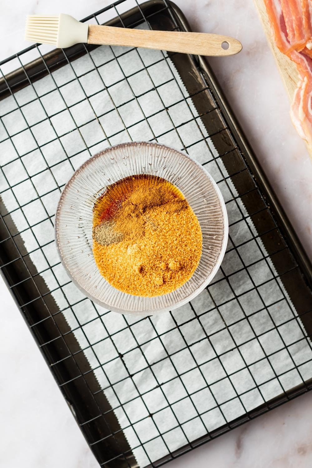 A bowl with brown sugar, maple syrup, and pepper on top of a wire rack on a baking sheet line with parchment paper.