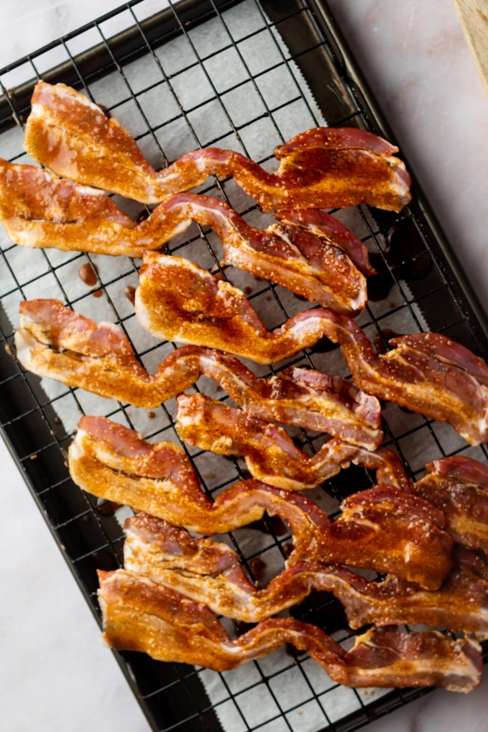 Eight slices of million Dollar bacon on a wire rack on a baking sheet lined with parchment paper.