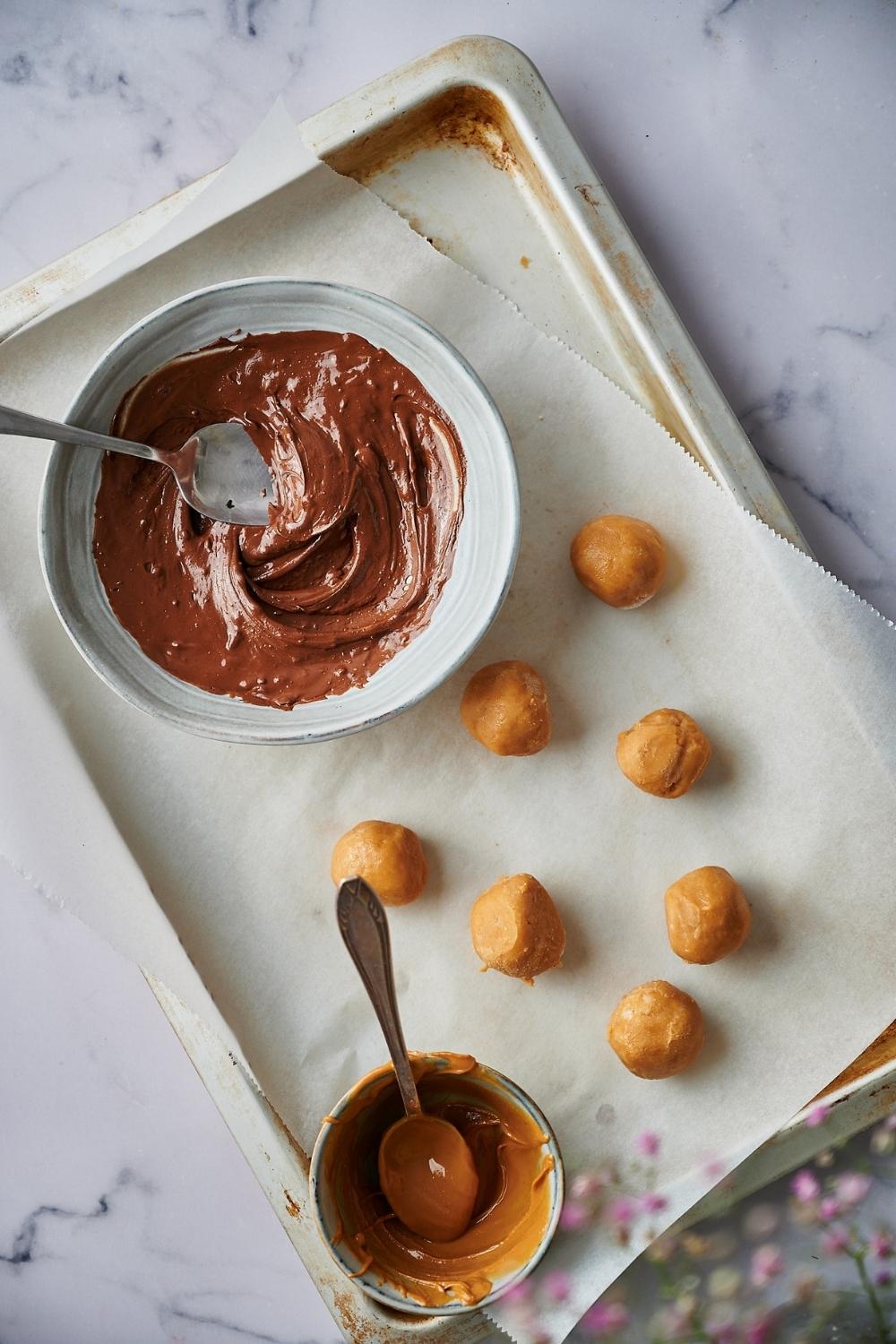 a bowl of melted chocolate next to a batch of uncoated peanut butter balls