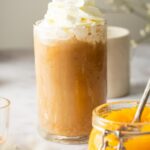 Pumpkin cream cold brew with whipped cream on top in a glass. In front of that is a glass filled with pumpkin puree.
