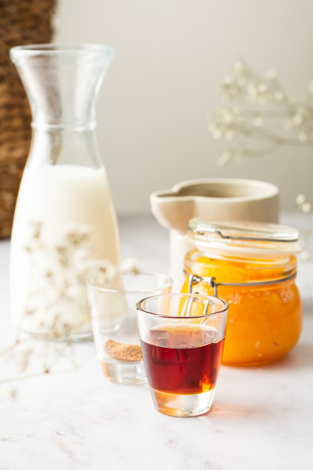 A jar of maple syrup, a glass of pumpkin pie spice, a glass of half and half, and a glass of pumpkin puree all on a white counter.