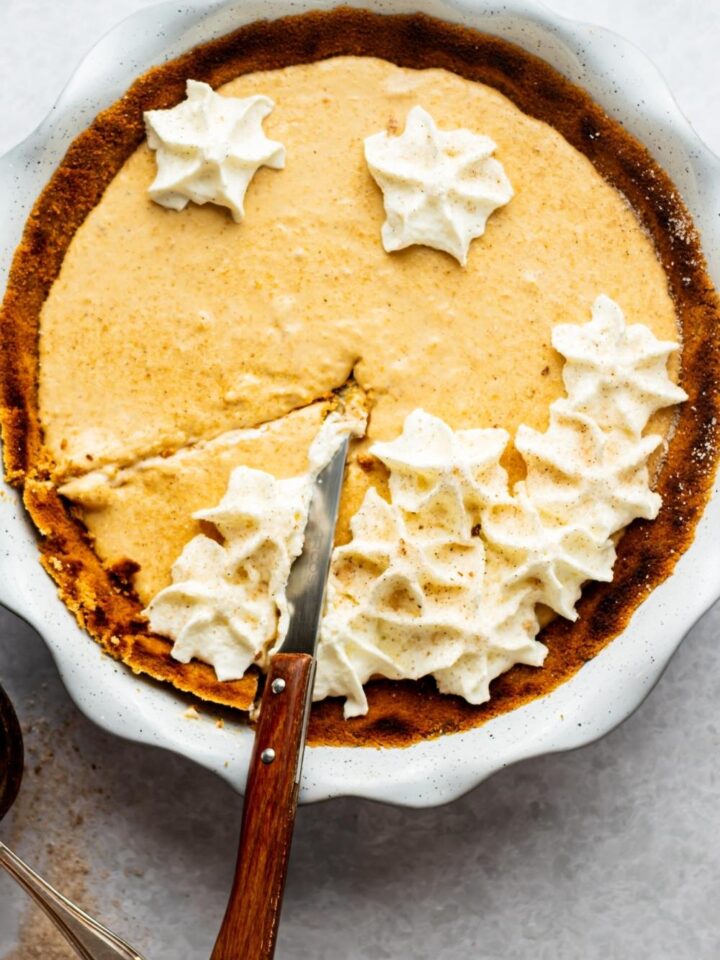 A no bake pumpkin pie with one slice cut in it with a knife on the slice in a pie dish.