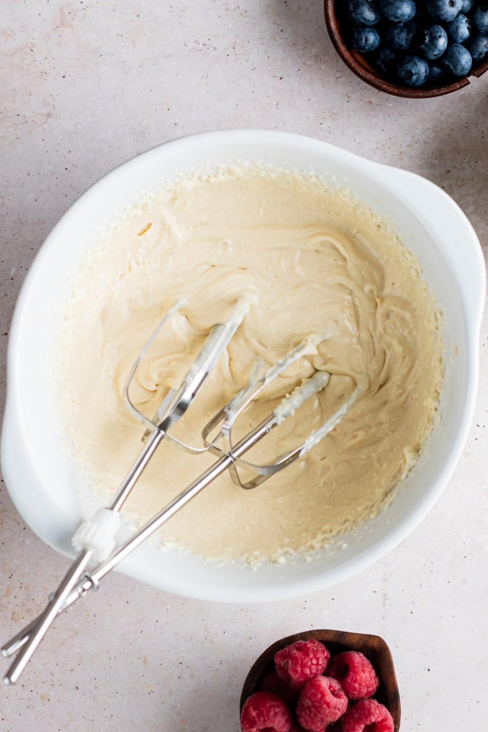 A mixing bowl with cheesecake filling and two beaters in it.