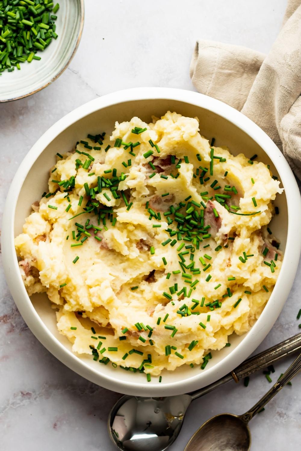 Green onion on top of Redskin mashed potatoes in a white bowl that is on a white counter.