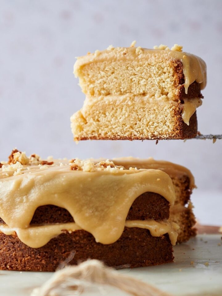 A slice of caramel cake being held of the whole caramel cake.
