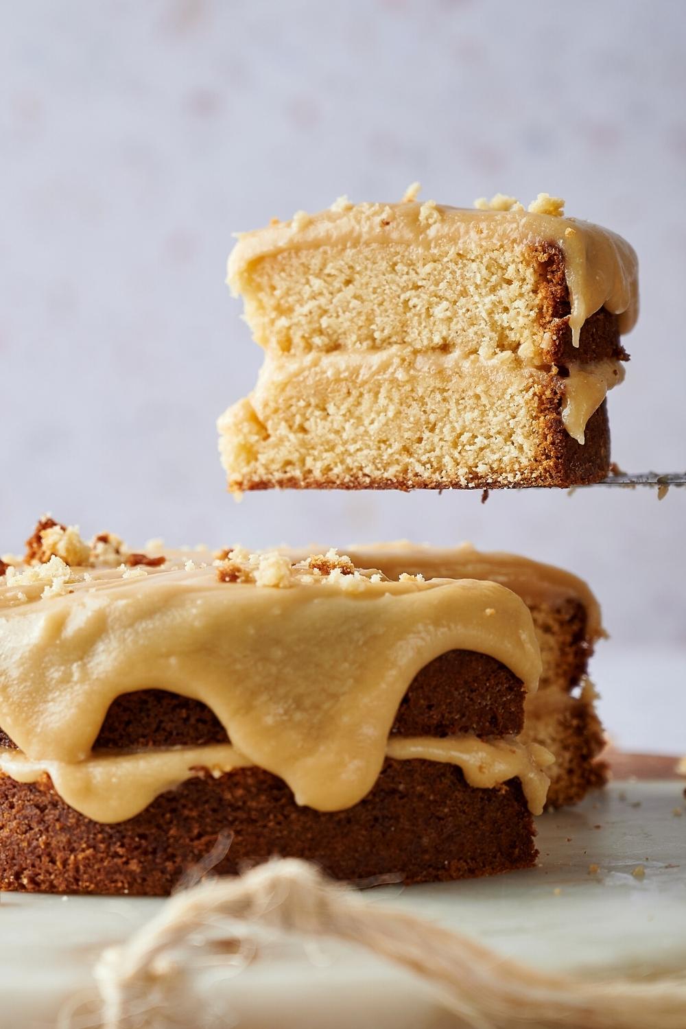 A slice of caramel cake being held of the whole caramel cake.