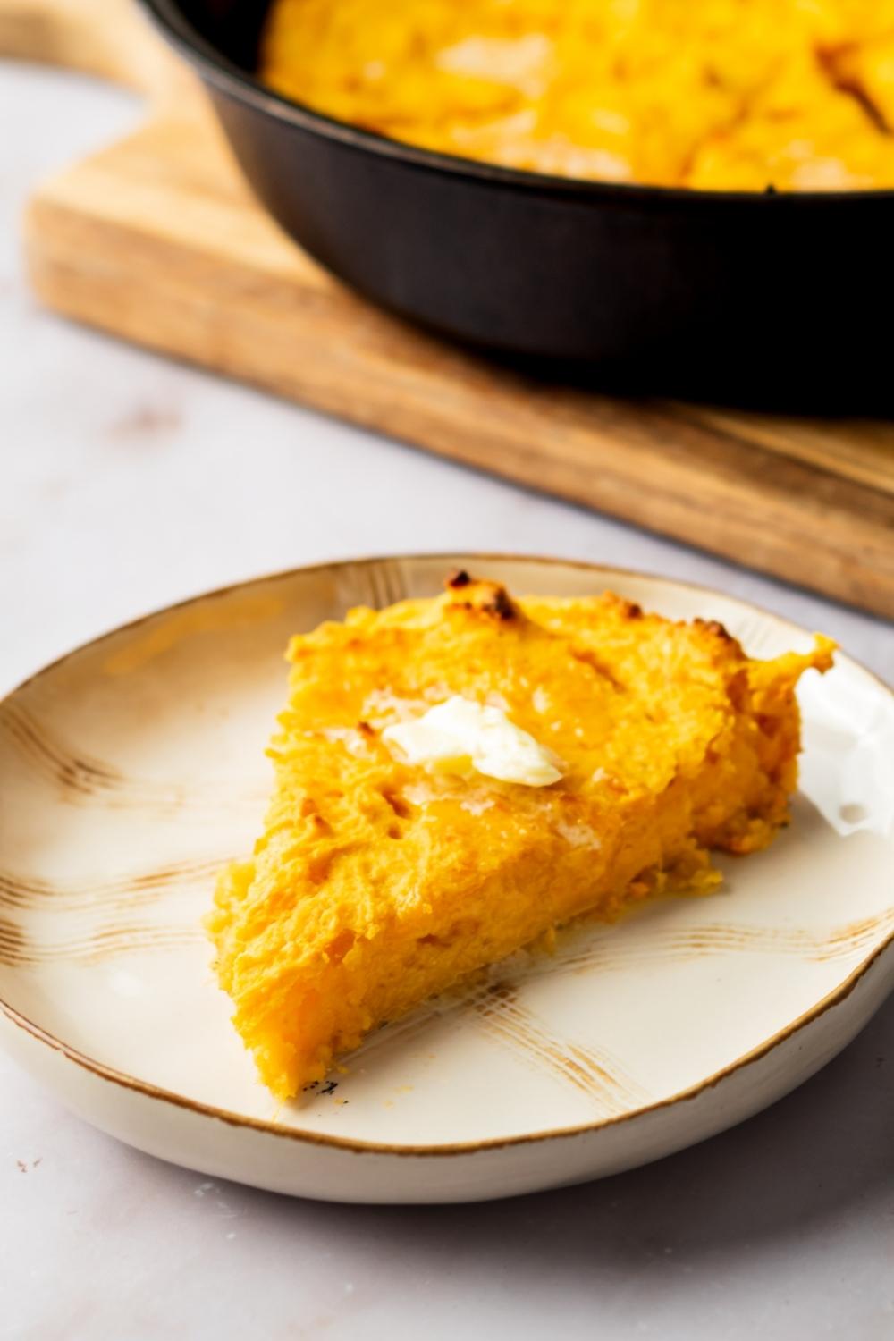 A slab of butter on top of a slice of sweet potato corn bread on a white plate.
