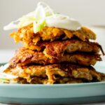 A dollop of sour cream on top of a stack of four sweet potato hash browns.
