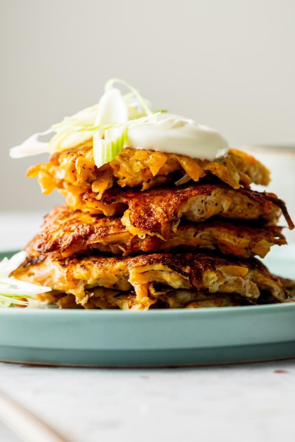 A dollop of sour cream on top of a stack of four sweet potato hash browns.