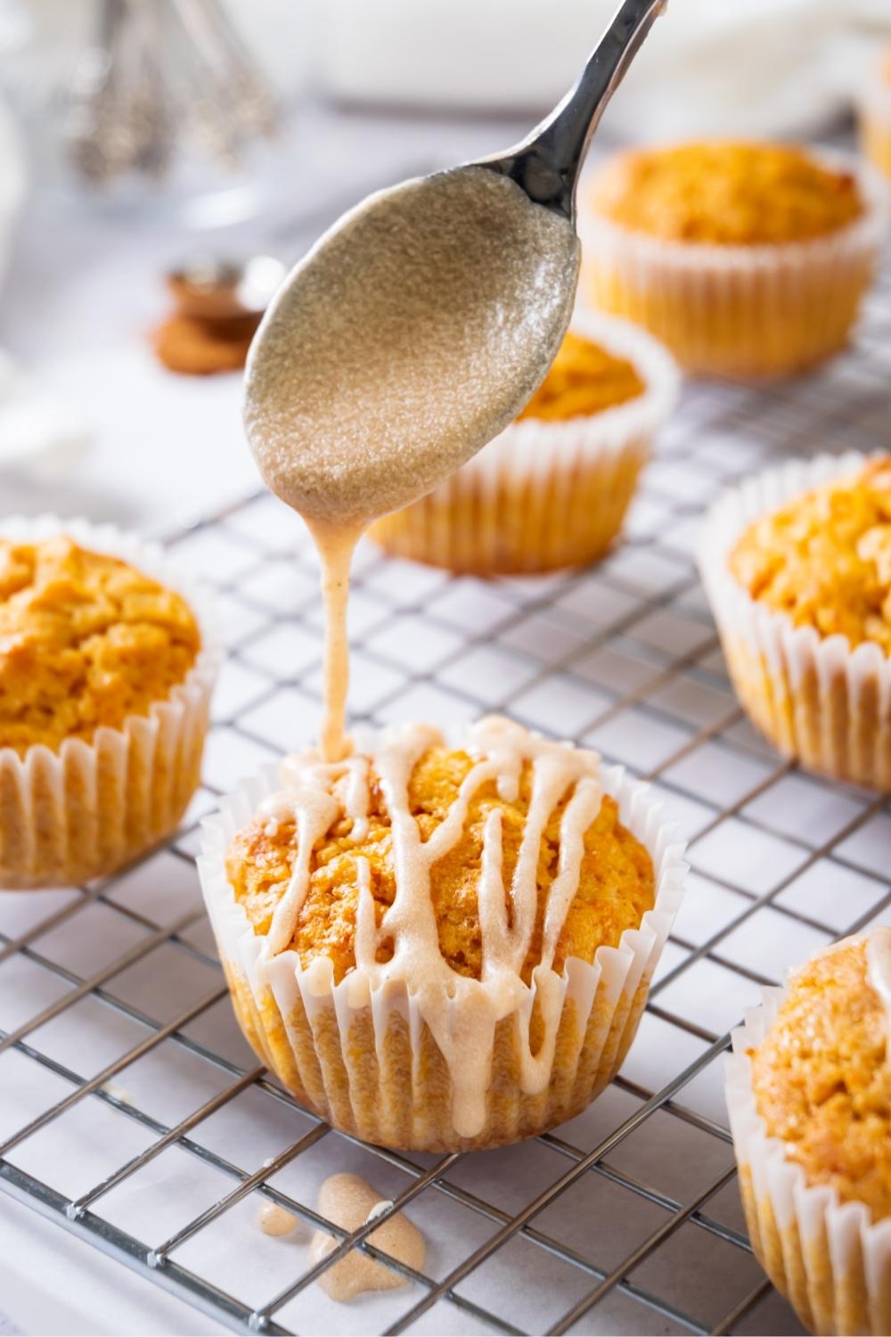 A spoon drizzling cinnamon sugar glaze on top of a sweet potato muffin on a wire rack.