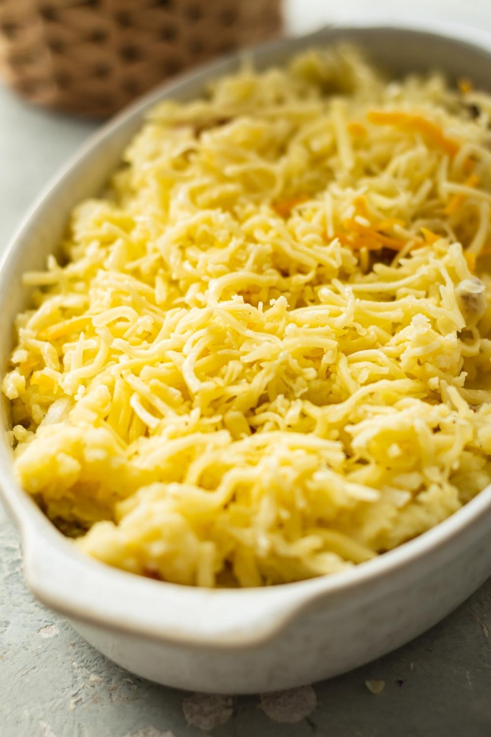 Shredded cheese on top of mashed potatoes in a casserole dish.