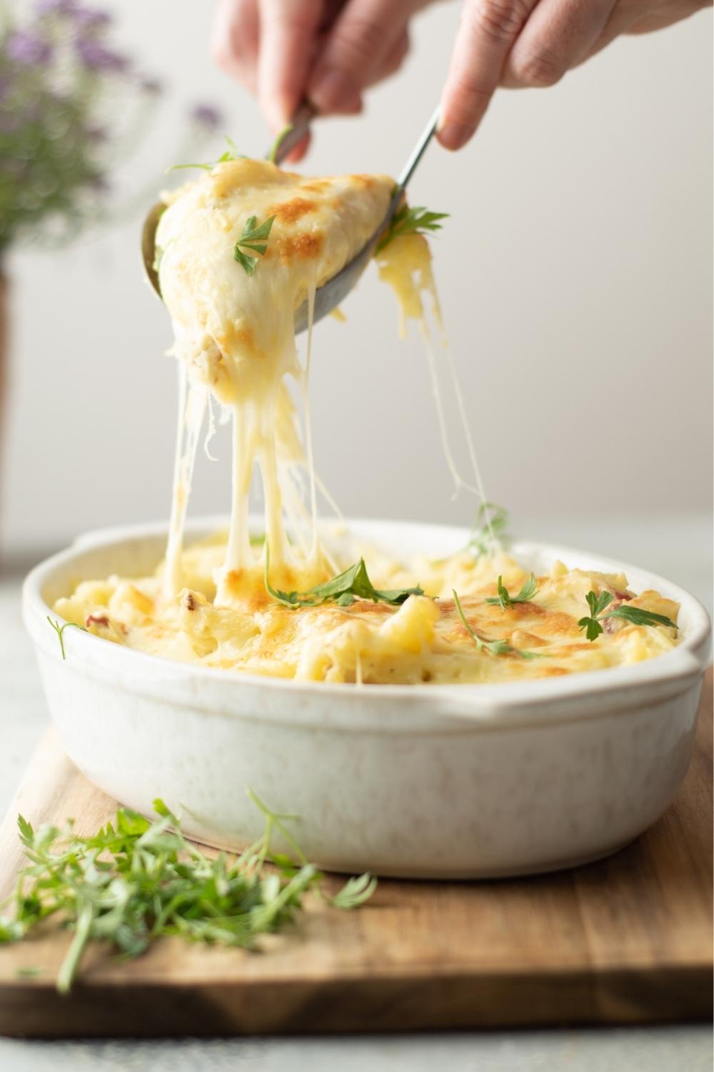 Two spoons scooping twice baked mashed potatoes from a casserole dish filled with the potatoes.