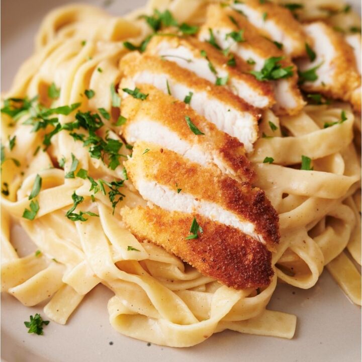 Chicken alfredo garnished with parsley on a white plate.