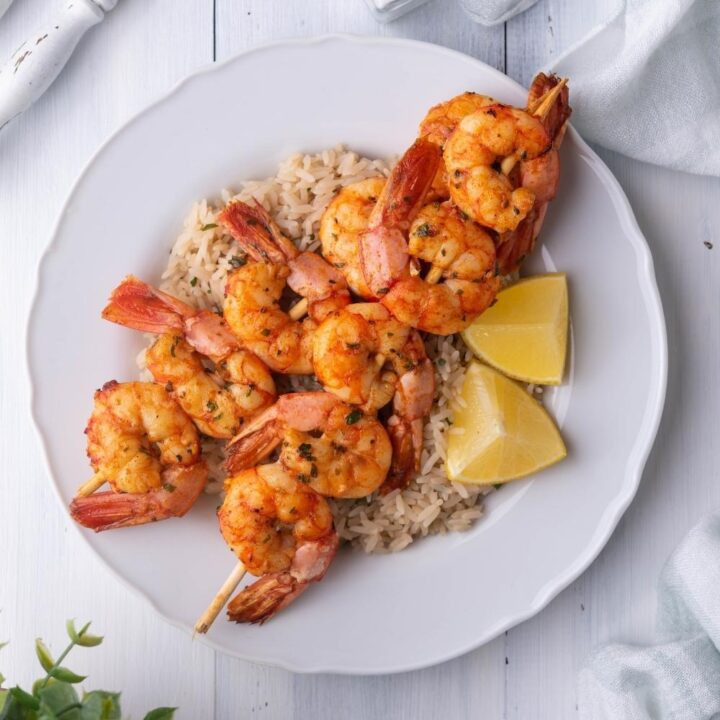 Texas Roadhouse grilled shrimp served over rice with lemon wedges, on a white plate surrounded by silverware, a napkin, salt and pepper.