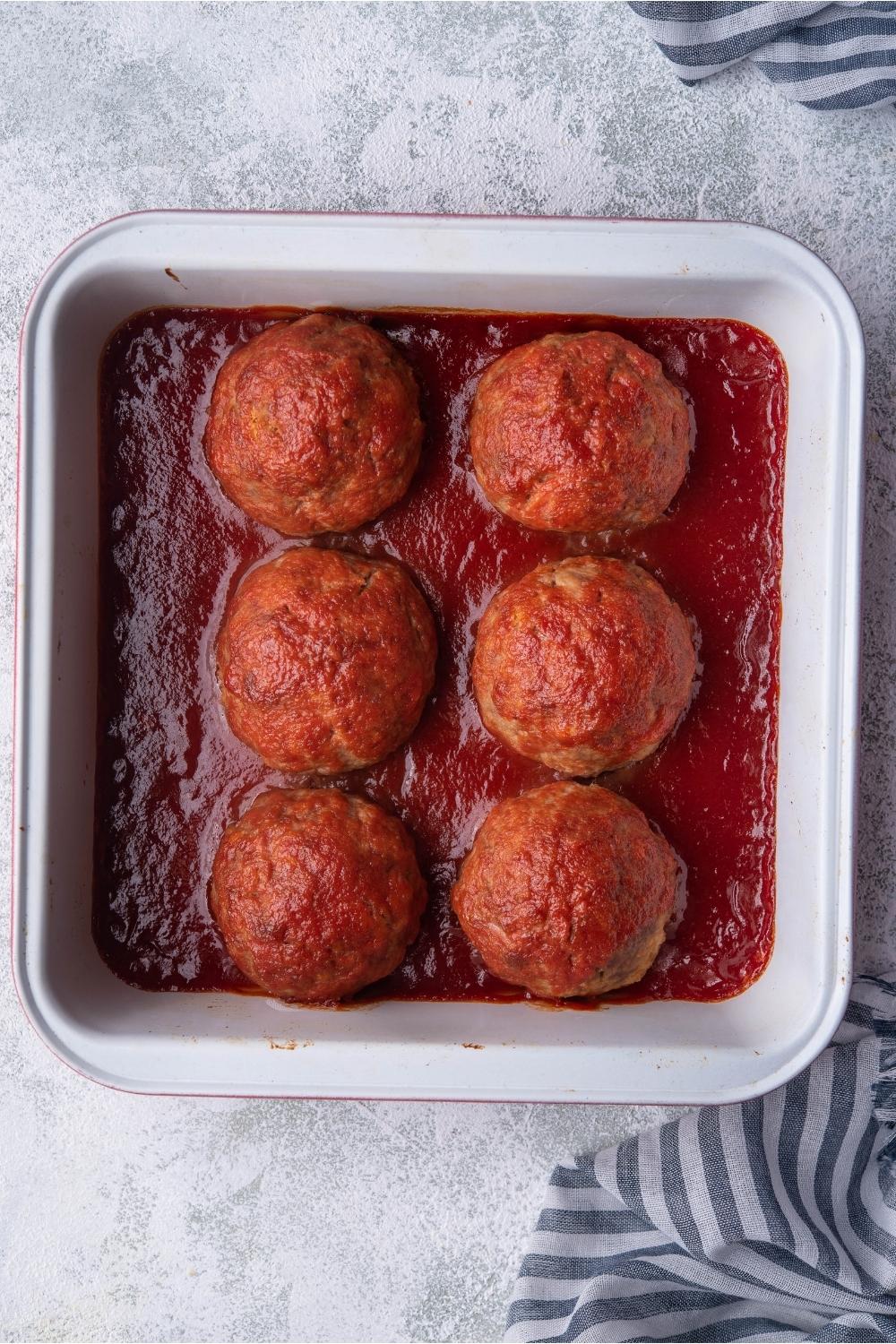 Baking dish with cooked ham meatballs covered in tomato sauce.