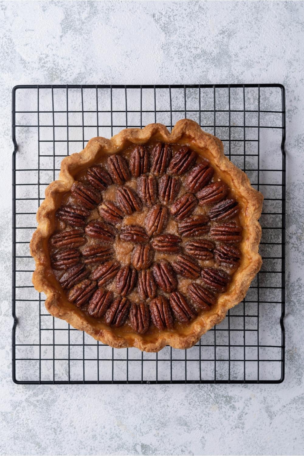 Freshly baked sweet potato pie with pecan topping cooling on a baking rack.