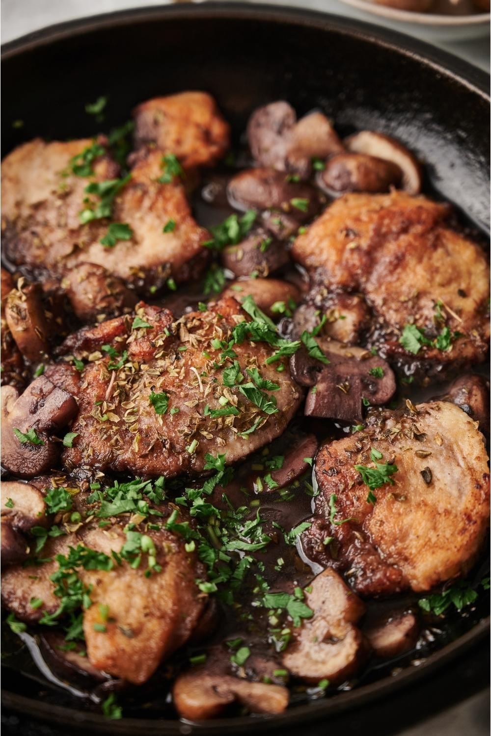Close up of cooked chicken marsala in a black cast iron pan, with fresh parsley on top to garnish.