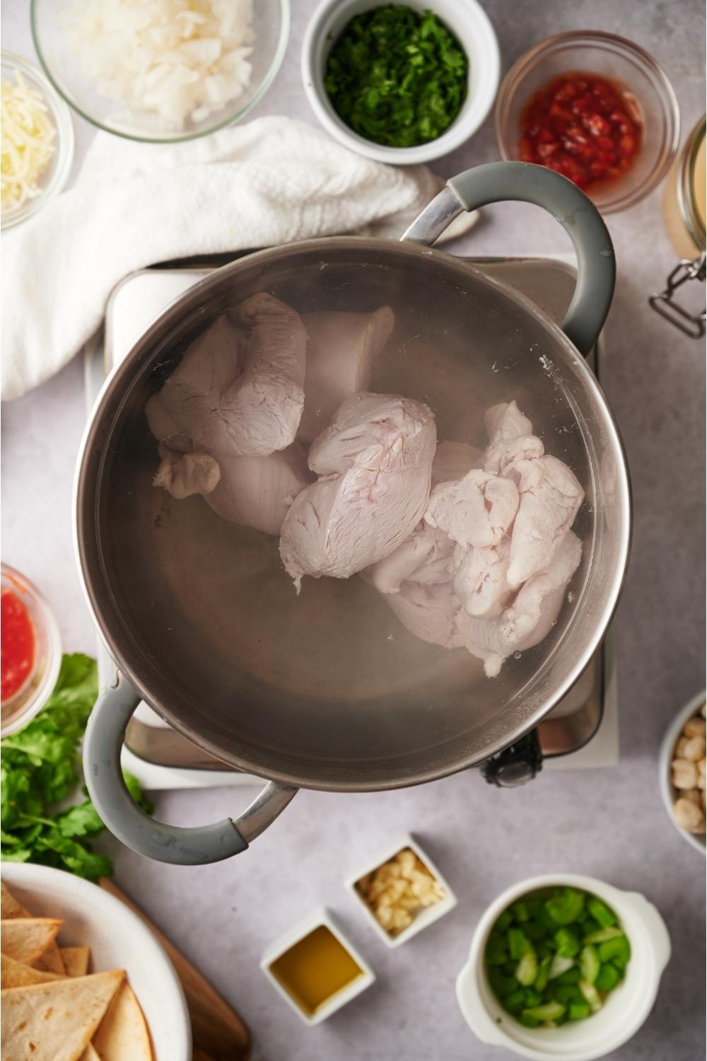 A pot of boiled chicken with ingredients to make southwest chicken soup including bowls of garlic, green chilis, and onion.