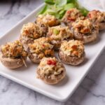 Red lobster crab stuffed mushrooms on a white plate with a garnish of greens.
