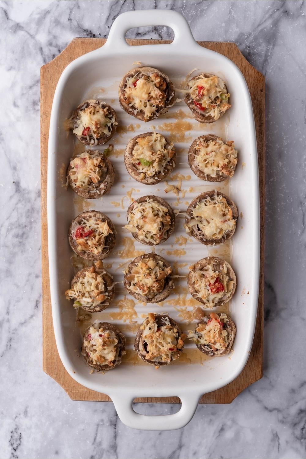 Red lobster crab stuffed mushrooms in a white baking dish on a wood board.