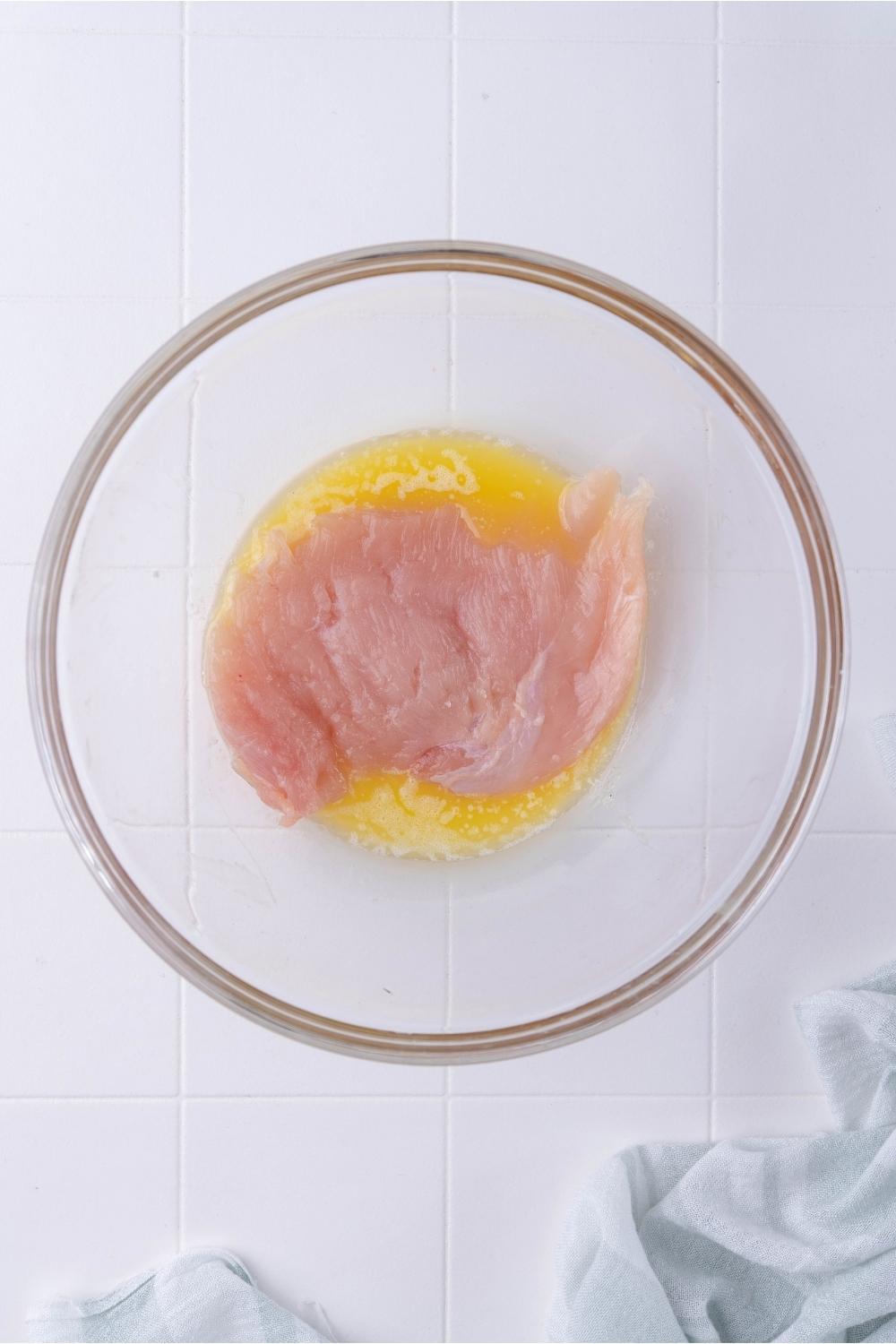 Clear bowl with raw chicken soaking in melted butter.