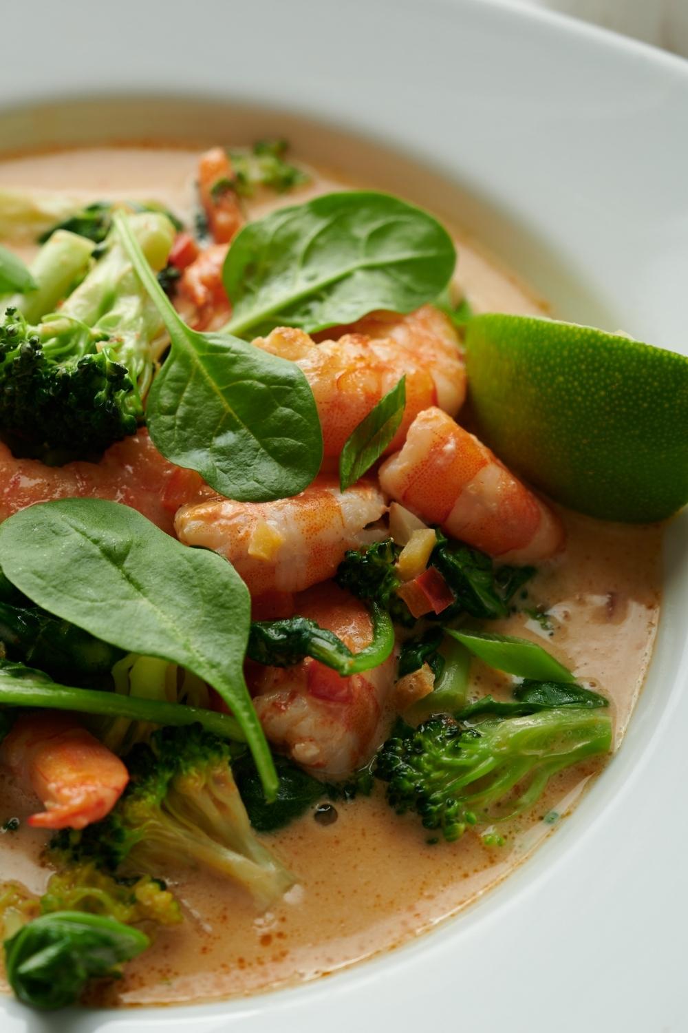 A close up of a serving bowl containing homemade curry shrimp. Garnished with cilantro and a lime.