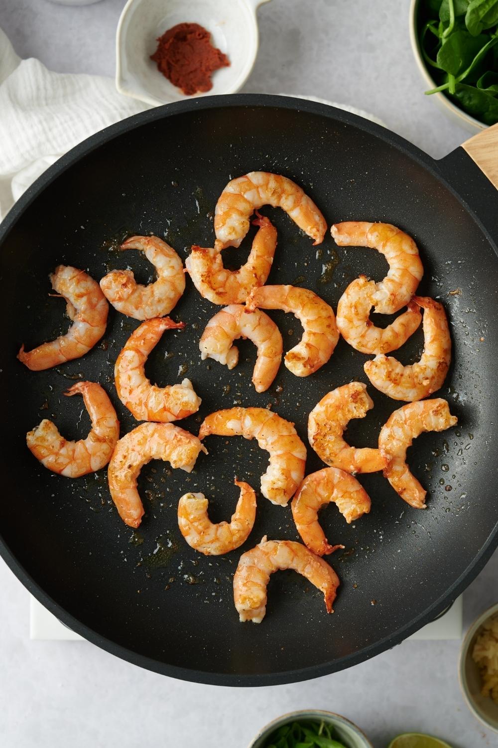 A hot pan with oil and cooked shrimp.