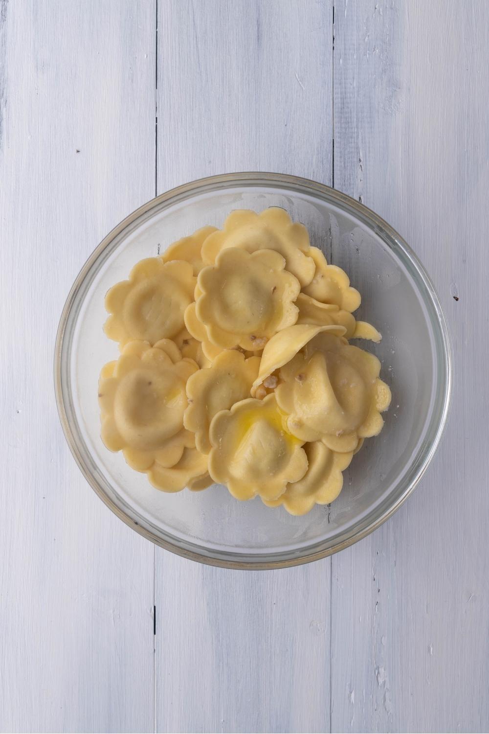 A clear bowl of cheese ravioli on a light blue counter.