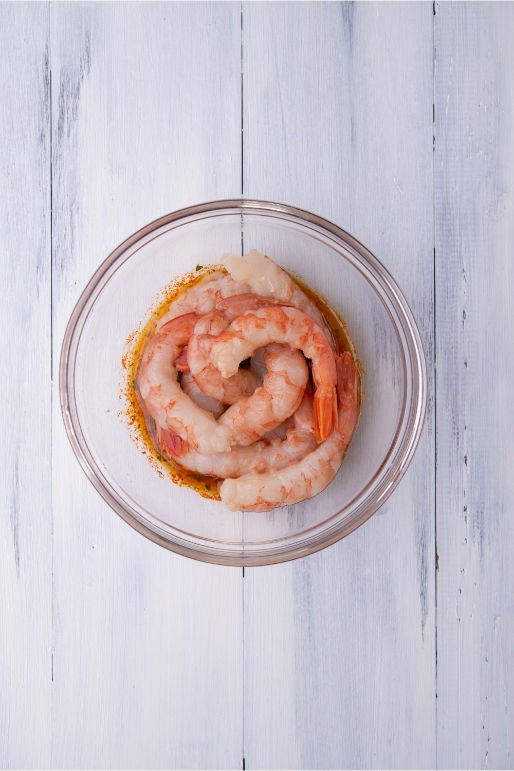 A clear bowl of raw shrimp in a marinade.