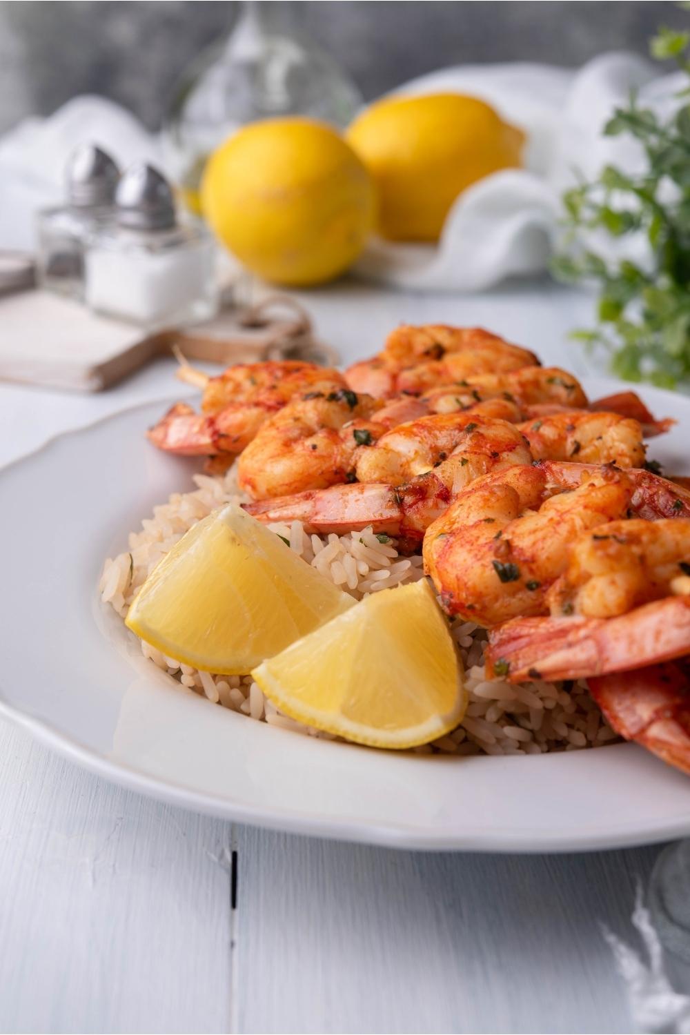 Texas Roadhouse grilled shrimp served over rice with lemon wedges, on a white plate with lemons in the background.