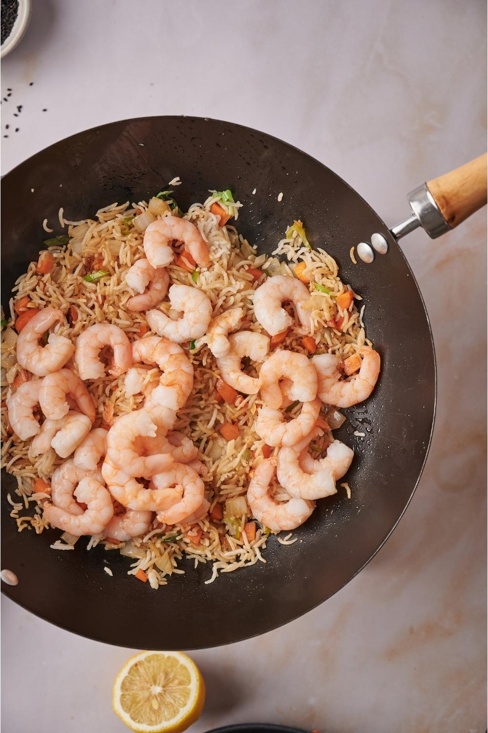 A skillet on a grey counter with Benihana fried rice and cooked shrimp freshly added with a lemon half next to the skillet.
