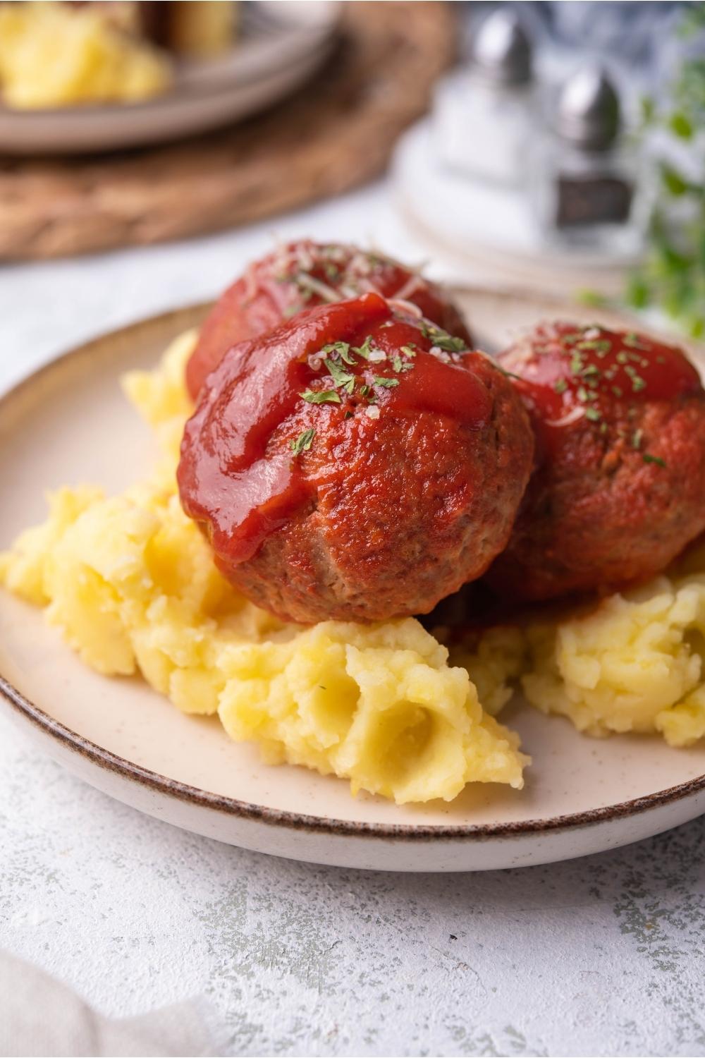 Ham balls covered in sauce on a white plate on top of mashed potatoes.