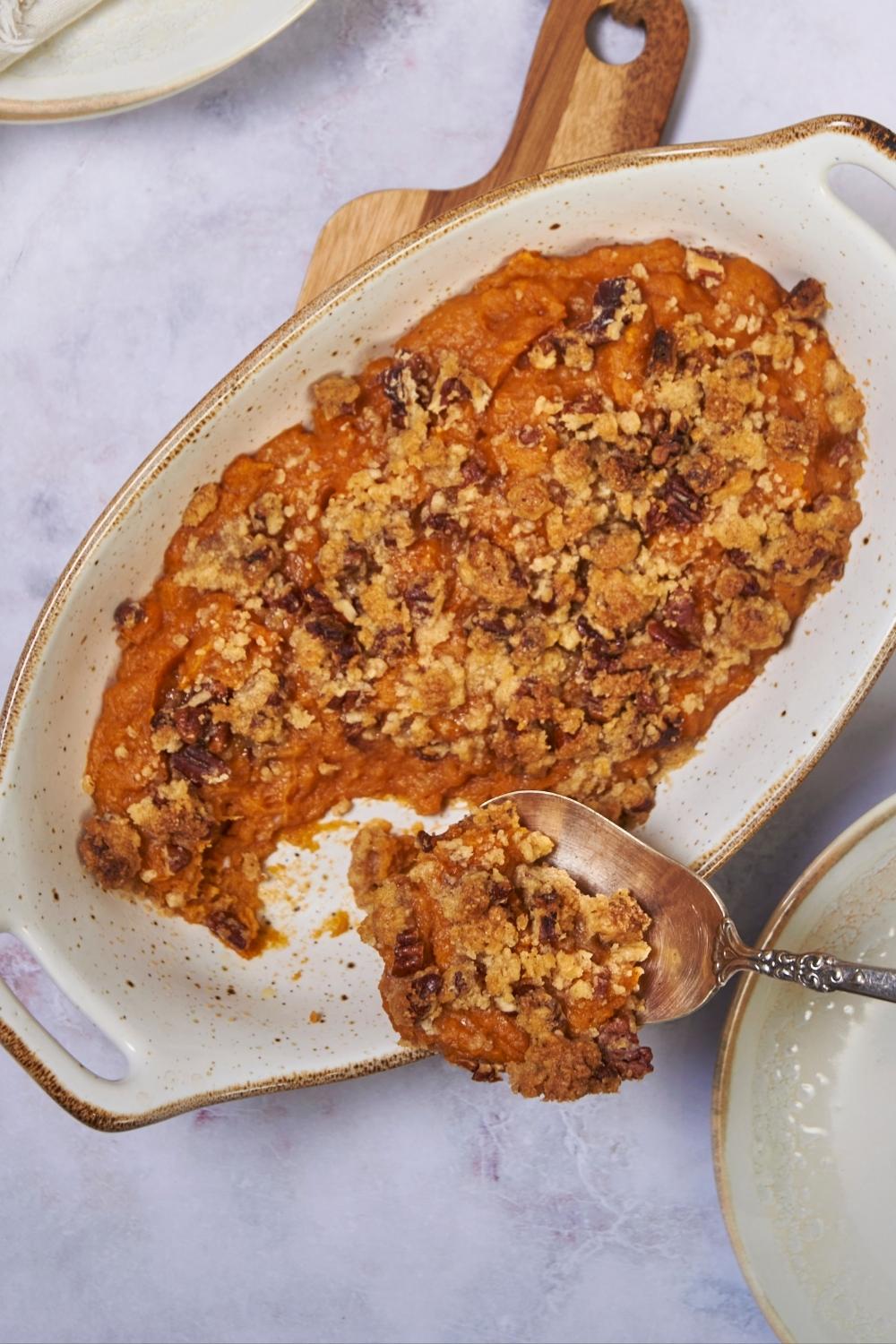 Ruth's Chris sweet potato casserole in a white baking dish with a serving being scooped out and put onto a plate.