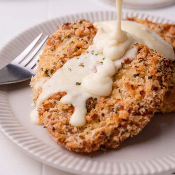 Texas roadhouse country fried chicken being covered in gravy. The chicken is on a white plate with a fork next to it.