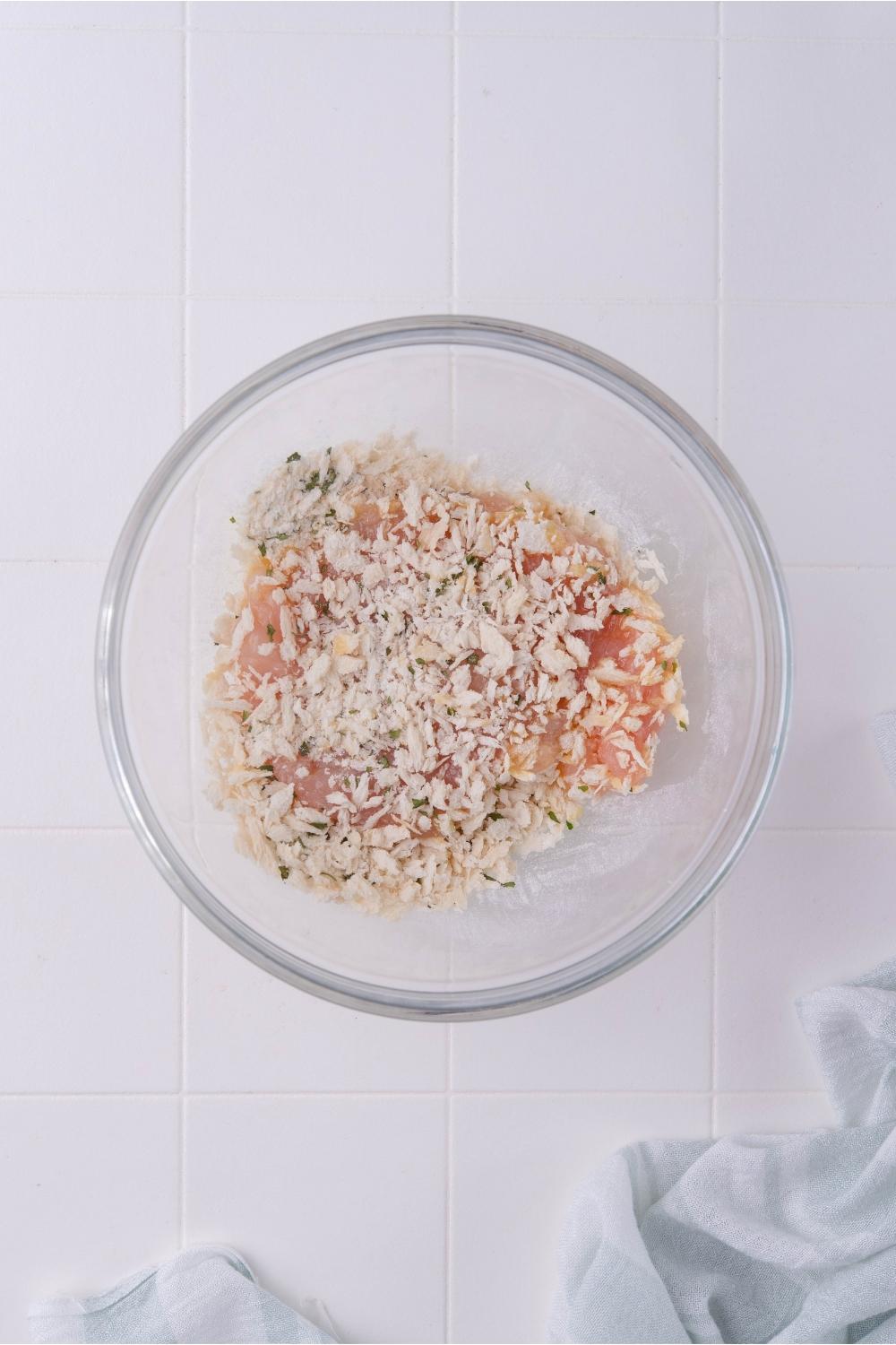 Clear bowl with raw chicken coated in a bread crumb mixture.
