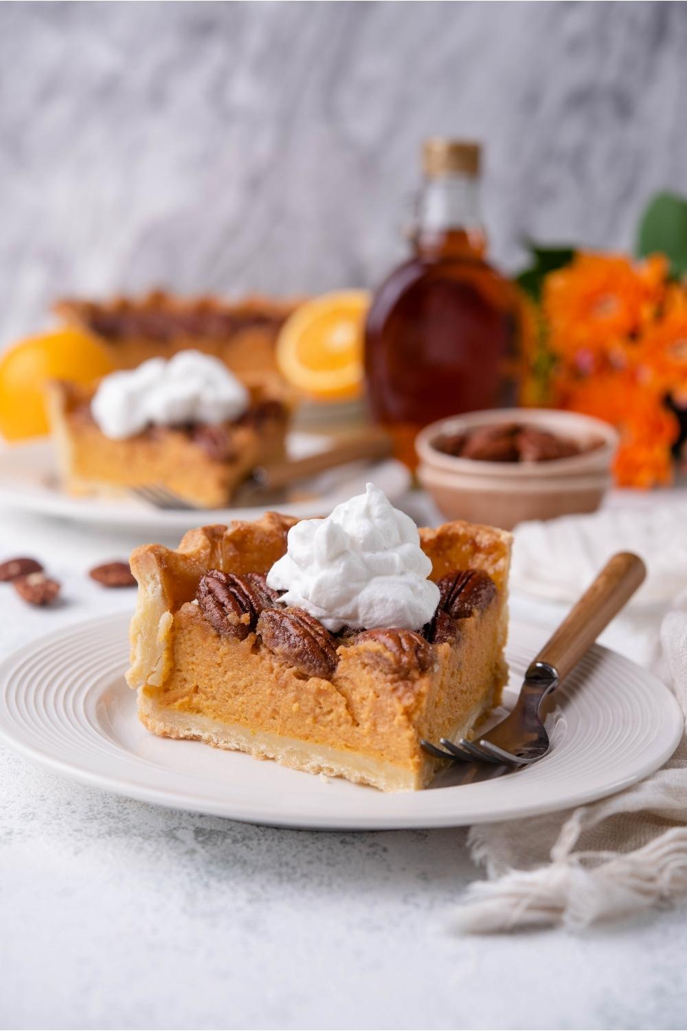 Slice of sweet potato pecan pie topped with whipped cream on a white plate with a fork. The rest of the pie is in the background.