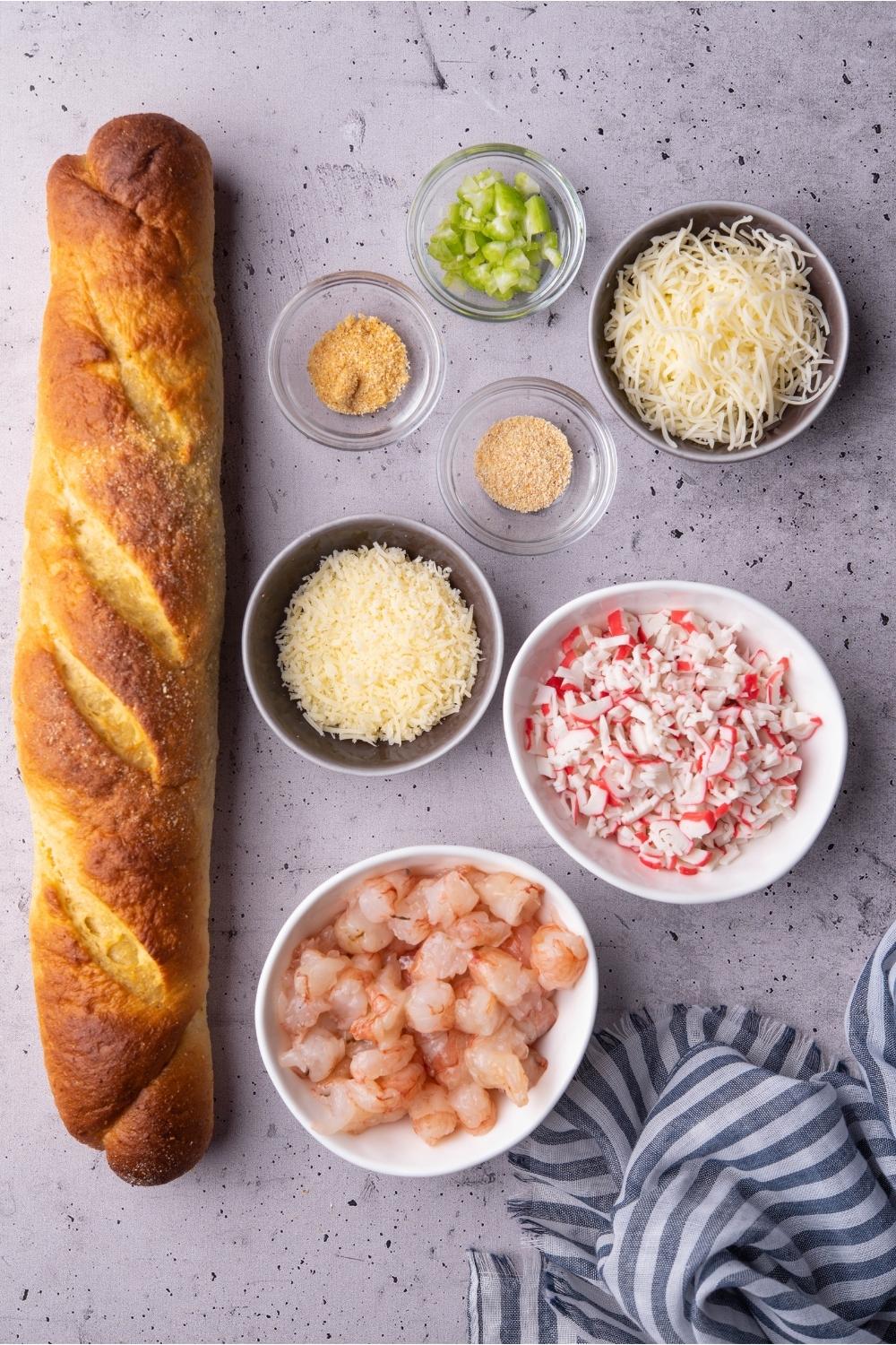 An assortment of ingredients for Vietnamese shrimp toast including a French baguette, uncooked shrimp, imitation crab, cheese, celery, and seasonings.