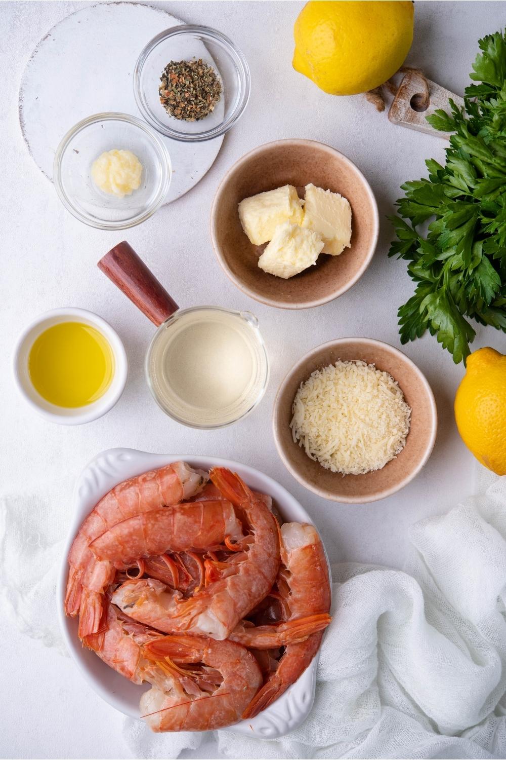 An assortment of ingredients to make shrimp scampi including bowls of raw shrimp, cheese, butter, seasonings, a lemon, and parsley.
