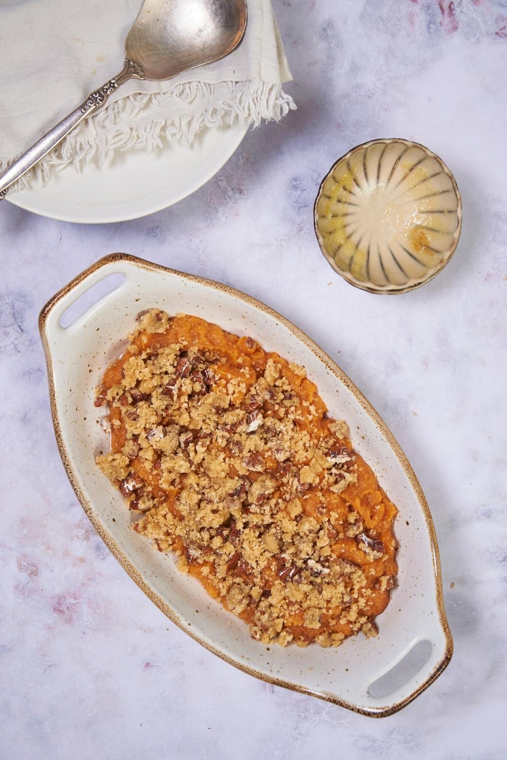 White baking dish with unbaked sweet potato casserole and a pecan crumble topping.