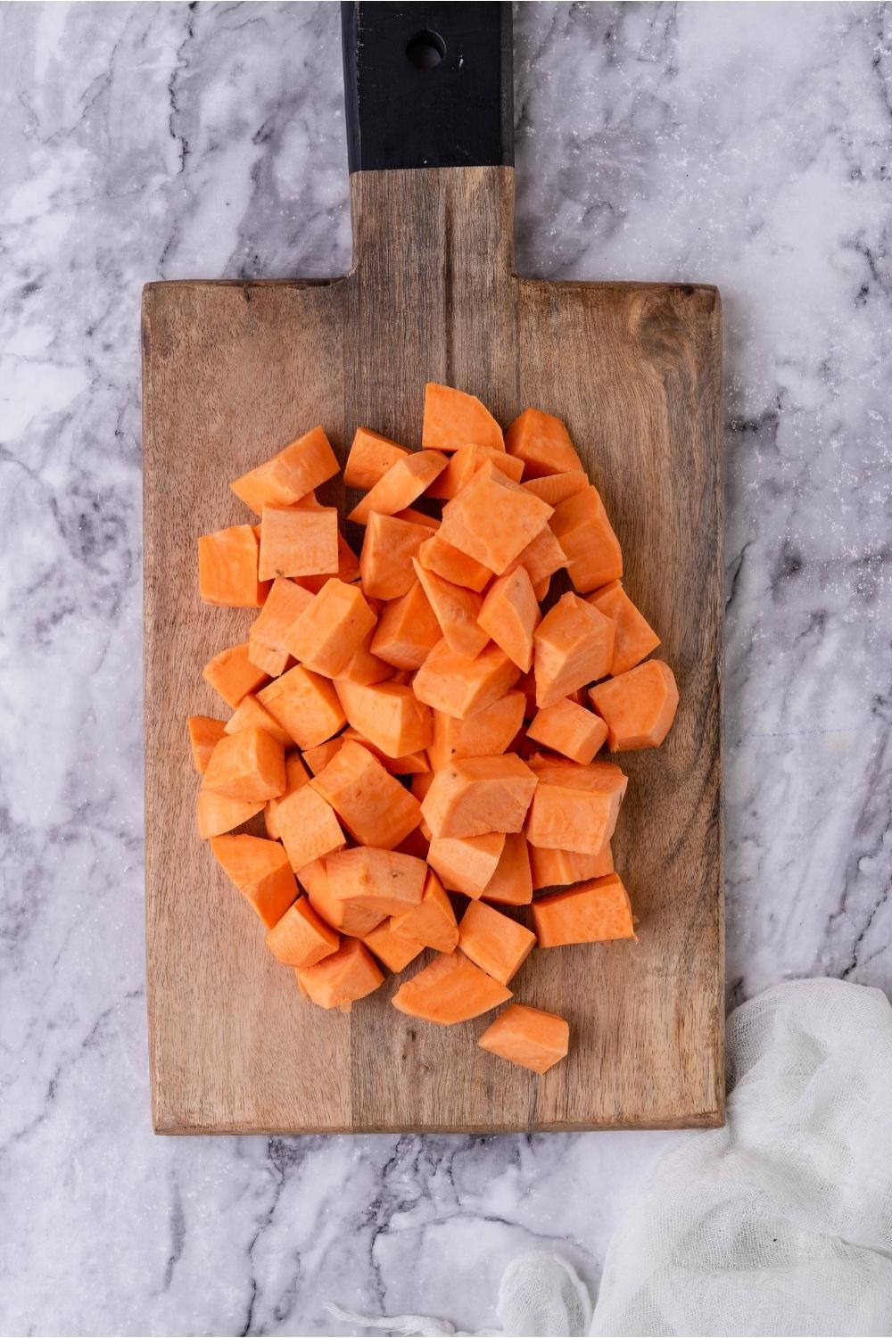 Sweet potato cubes on a wood cutting board.