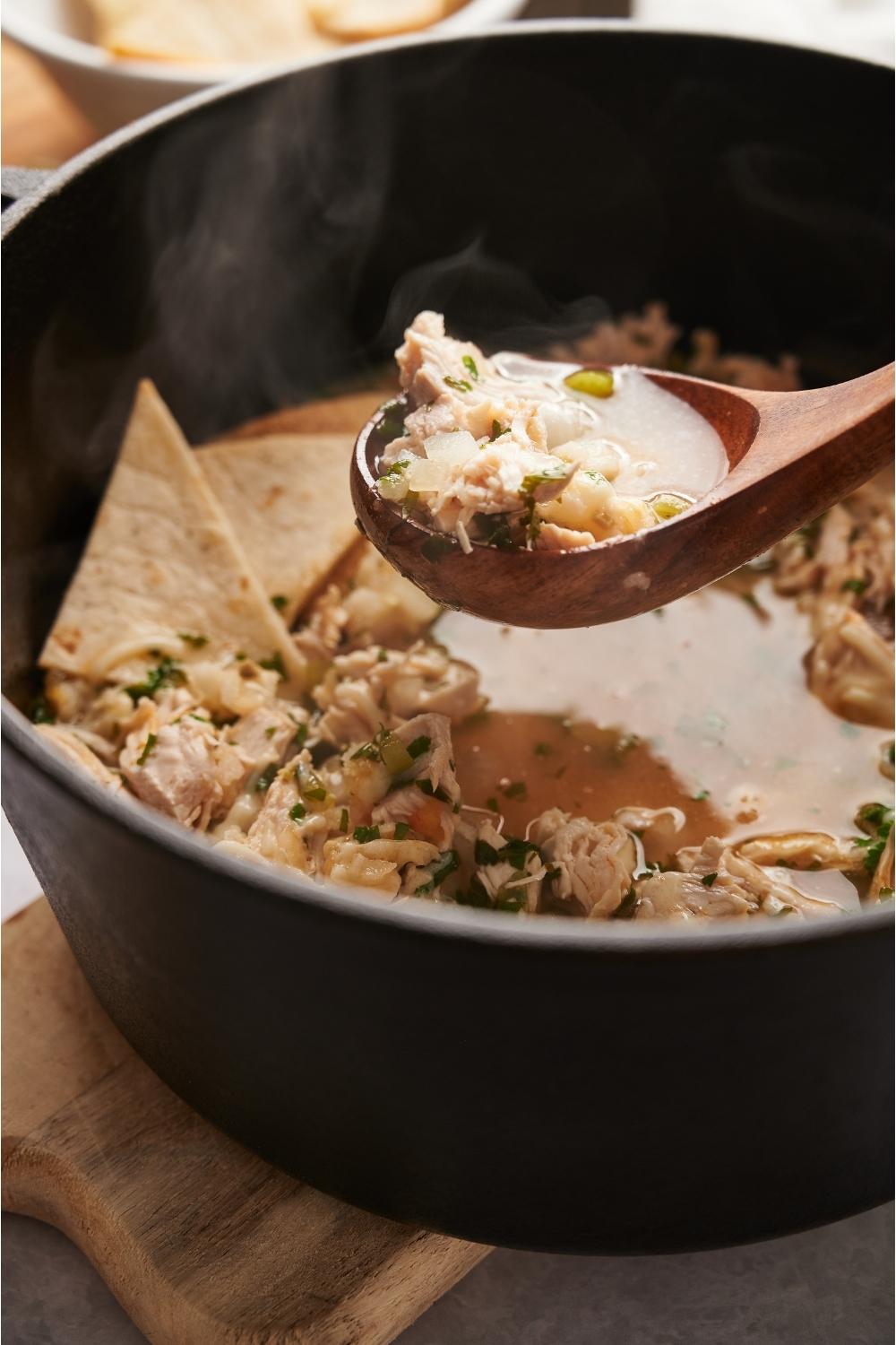 A spoon scooping from a bowl of Chili's southwest chicken soup in a dutch oven.