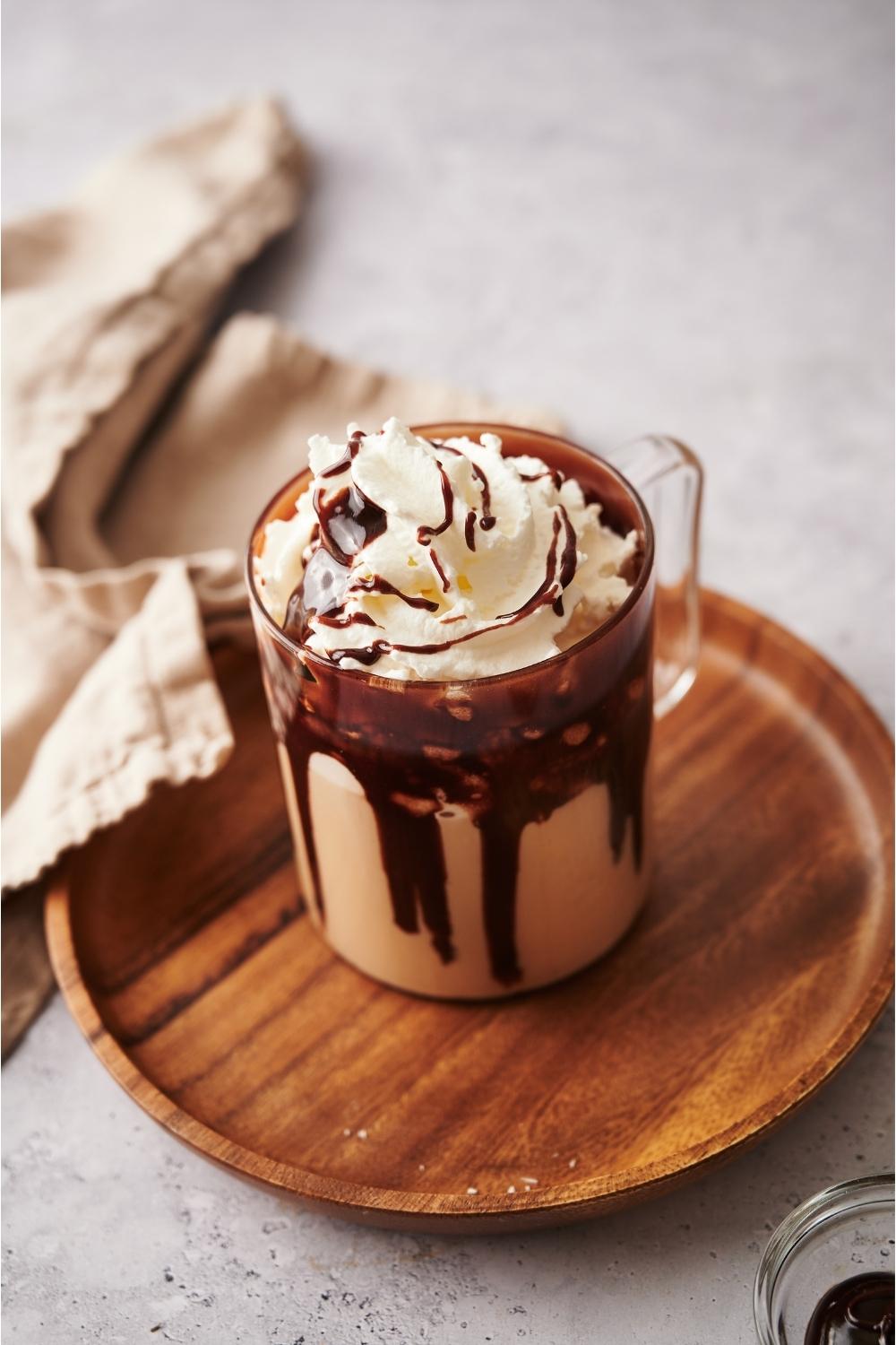 A cafe mocha in a glass mug on a wooden plate.