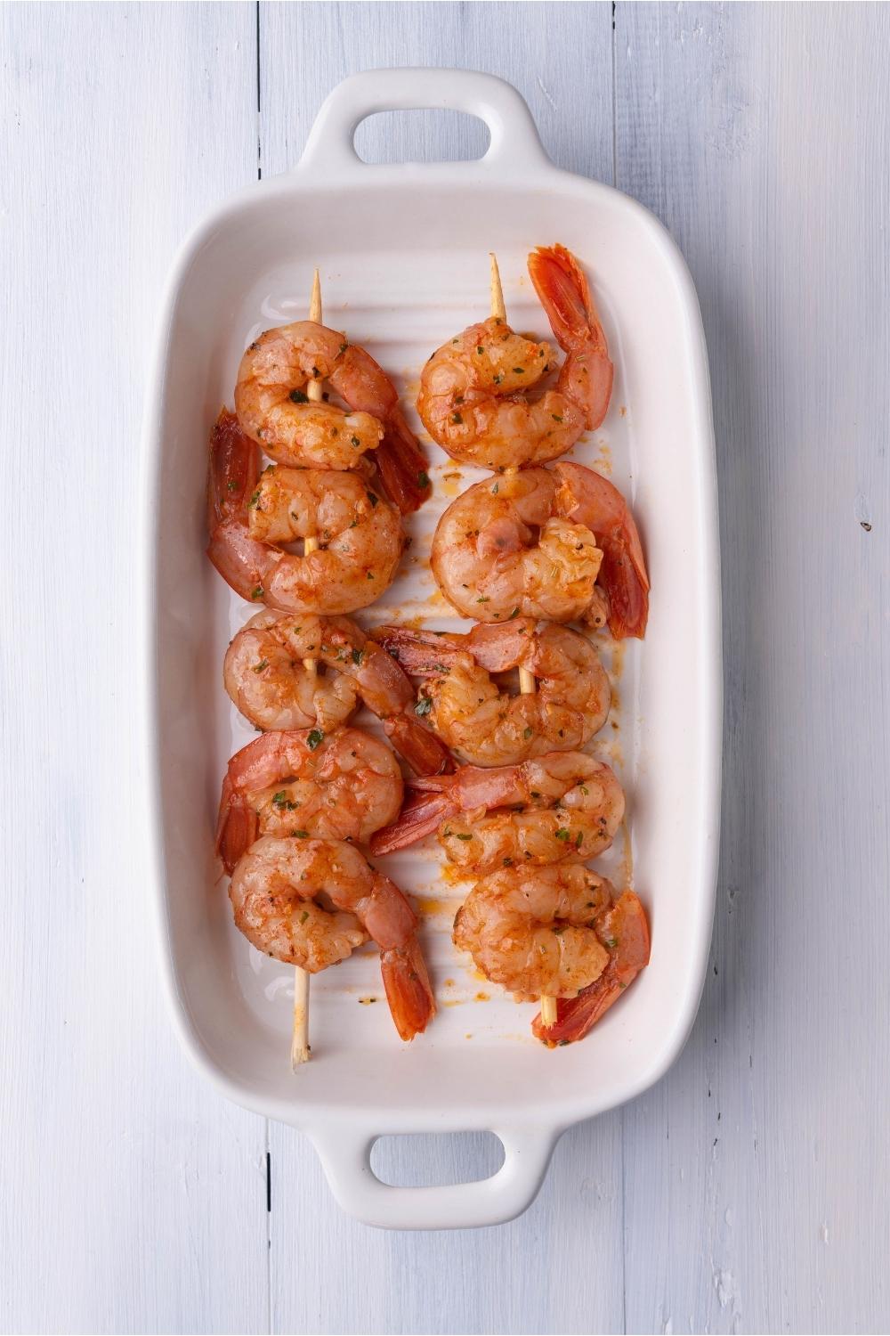 Marinated shrimp skewers in a white grill pan.