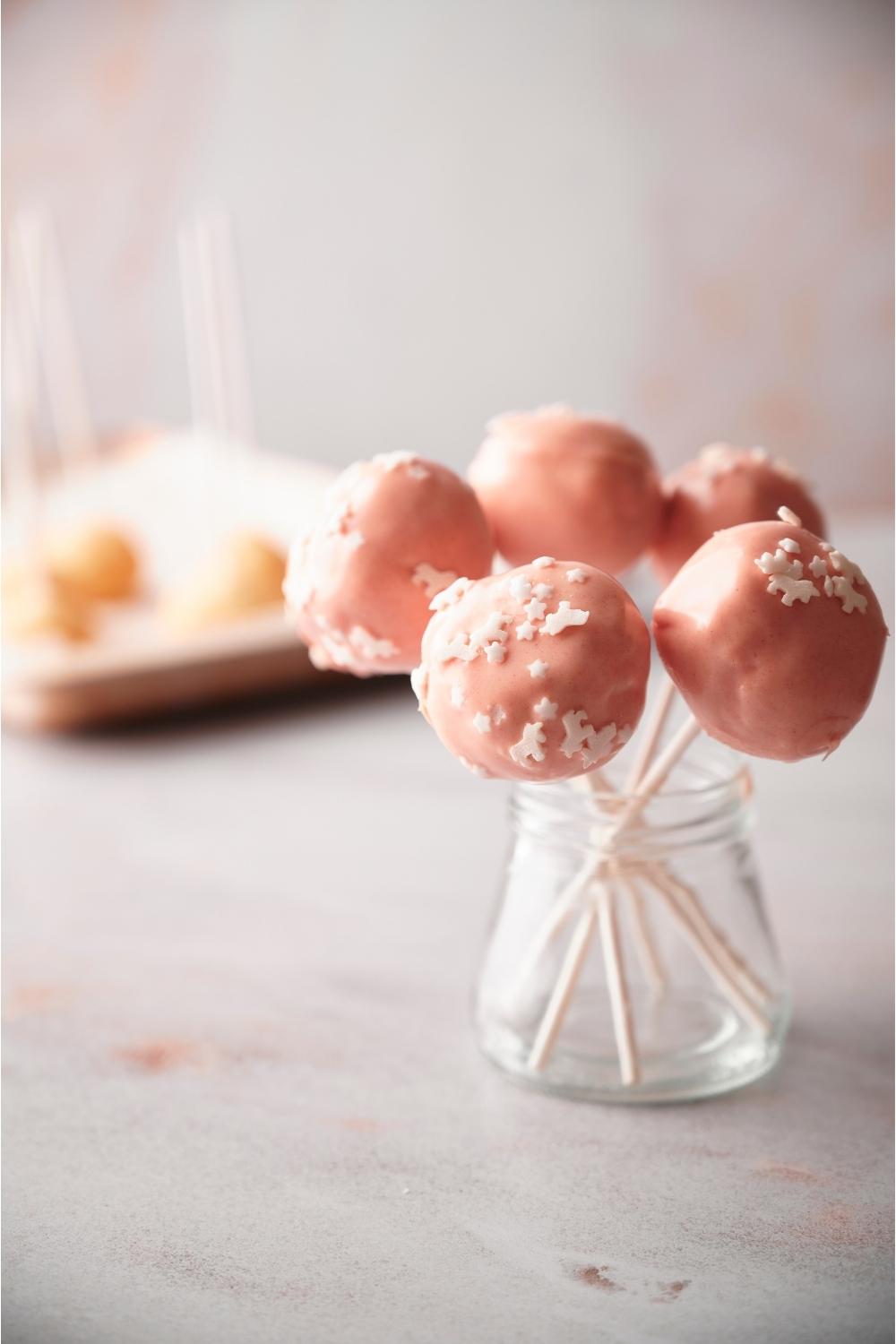 Starbucks cake pops in a clear jar with more cake pops in the background.